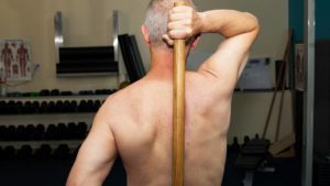 fit older man with fitness dowel on bare back on spine and muscle